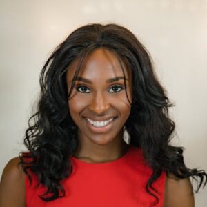 Confident woman smiling in a red dress, captured indoors with a warm, modern feel.