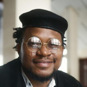 Confident man in glasses with a stylish hat smiling indoors.